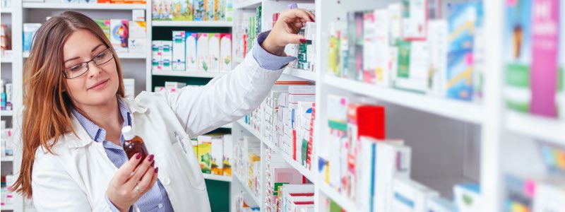 Female pharmacist filling prescription from shelf of pharmacy