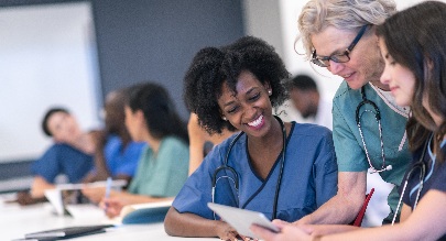 several women in scrubs sitting together at a table discussing what they are looking at on a tablet