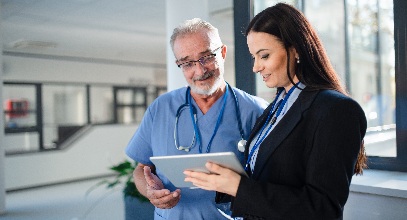 man wearing scrubs and a stethoscope and woman in a suit having a discussion in a hallway