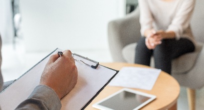a person's hand resting on a clipboard and is sitting across another person with a table in between them