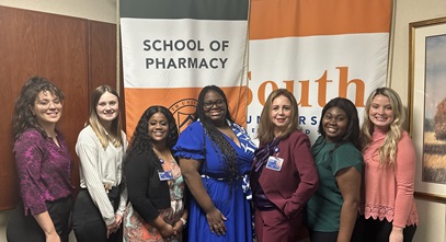 Group of School of Pharmacy women posing in front of the shool's logo