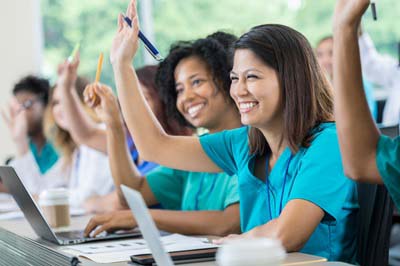 Nursing students in a classroom setting raising their hands