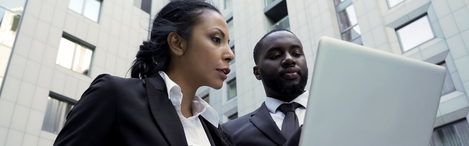 one african american woman in a dark suit and white shirt is pointing at a laptop and speaking with an african american man in a dark suite and tie