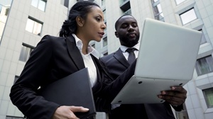 one african american woman in a dark suit and white shirt is pointing at a laptop and speaking with an african american man in a dark suite and tie
