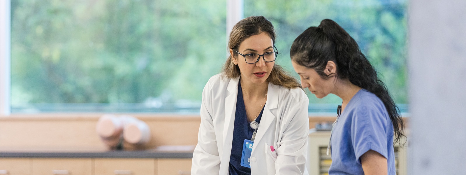 2 female healthcare workers in blue scrubs discussing information they are looking at on a clipboard
