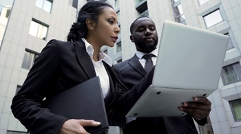 an african american woman and man conversing outside a building looking at the screen of a laptop