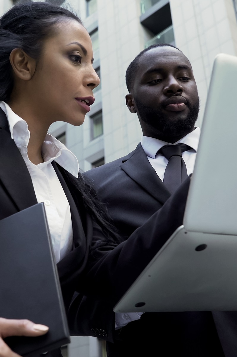 an african american woman and man conversing outside a building looking at the screen of a laptop