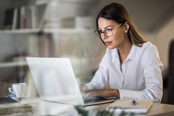 woman sitting at a desk with a coffee cup typing on her laptop