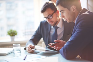 two men discussing what they are looking at on a tablet 