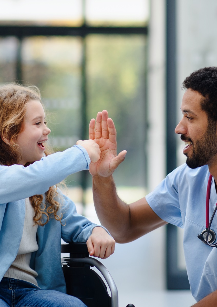 small female child in a wheelchair high fiving with a male nurse