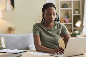 african american woman in military uniform tshirt sitting at a desk typing on a laptop