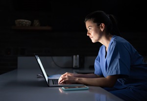 young woman in scrubs typing on a laptop