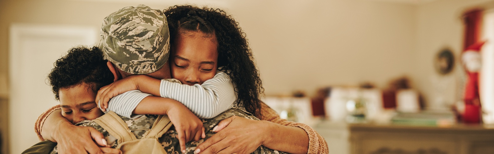 man in a military uniform wearing a backpack hugging 2 kids, one boy and one girl