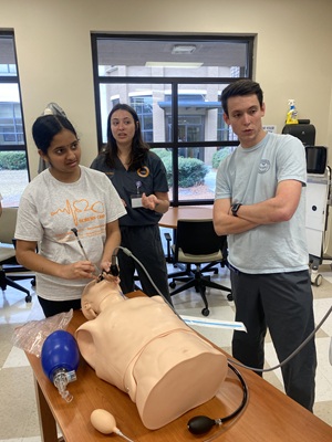 a female high school student practicing a nursing procedure with two South instructors overseeing