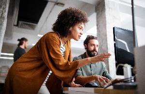 a woman and a man having a discussion as they look at a computer screen together