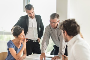 three men and one woman surrounding a table discussing what they are looking at