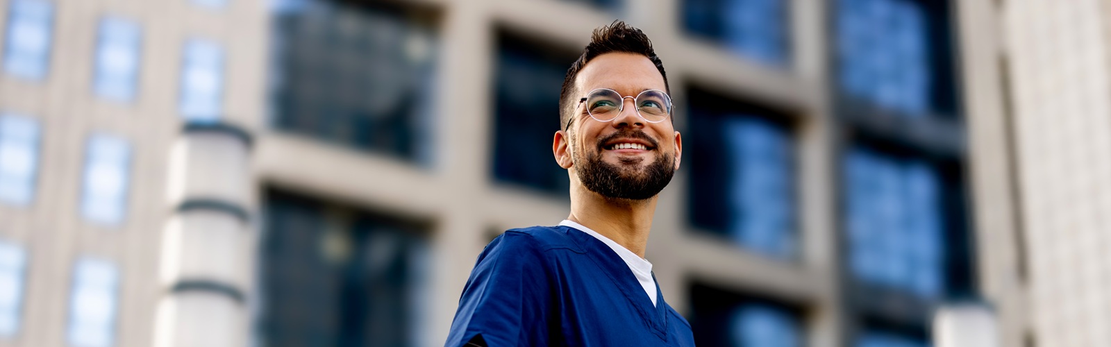 man wearing blue scrubs standing in front a building