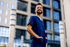man wearing blue scrubs standing in front a building