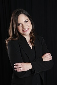 Laura Giraldo headshot in a black suit with arms crosses smiling at the camera