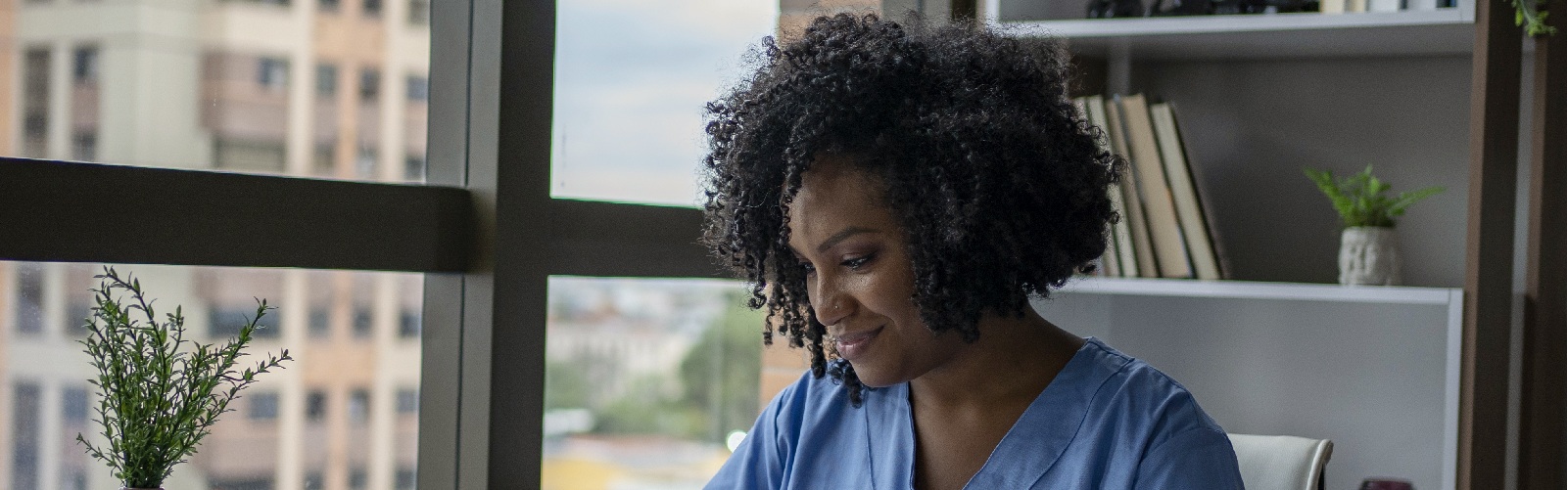 african american woman in scrubs sitting at a desk looking at her phone
