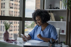african american woman in scrubs sitting at a desk looking at her phone