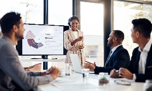 Woman giving presentation to 3 men in leadership meeting