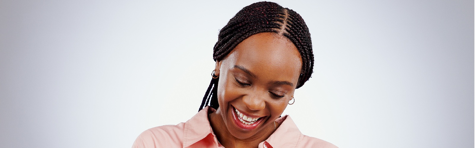 african american woman wearing a pink button down shirt smiling while writing in a notebook