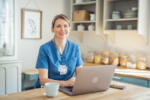 nurse in scrubs sitting at a desk in front of a laptop