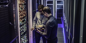 two men standing in a server room looking at a tablet