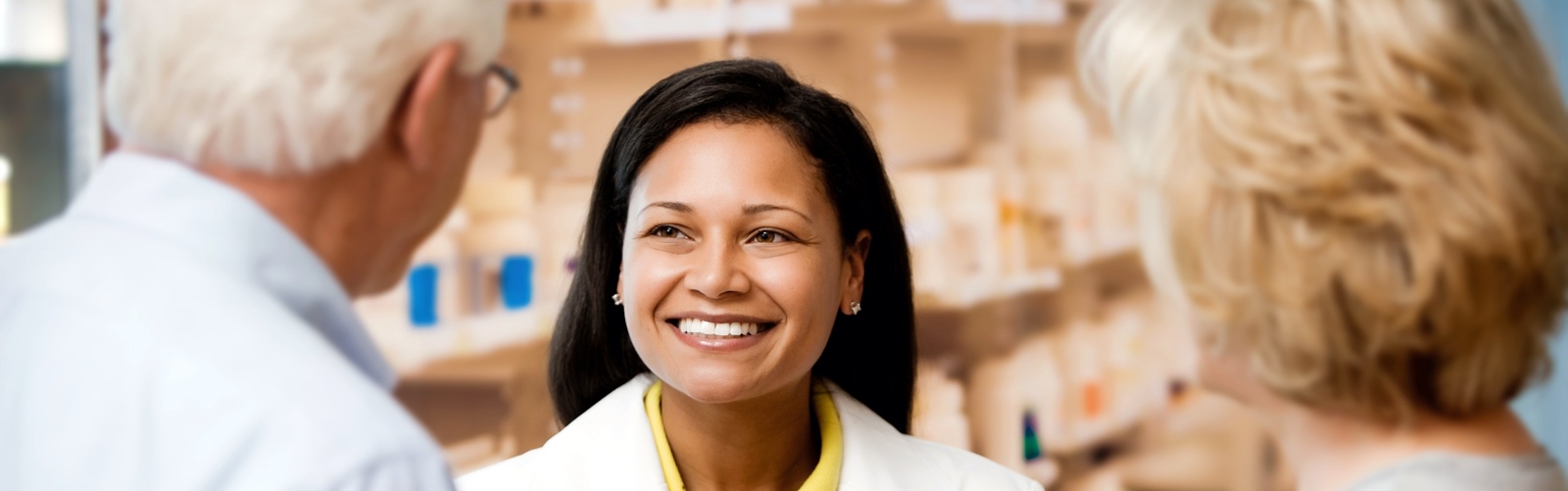 female pharmacist speaking with two older people at the pharmacy counter