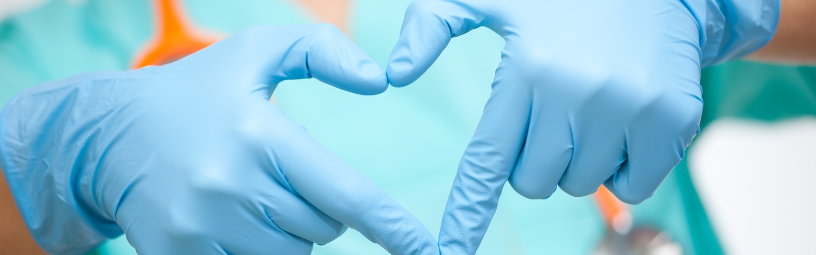 a person in blue scrubs making the heart symbol with both hands