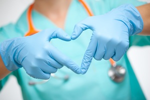 a person in blue scrubs making the heart symbol with both hands