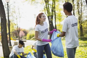 two young men and one woman picking up trash in a park wearing white t-shirts that say volunteer