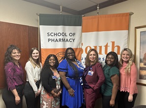 Group of School of Pharmacy women posing in front of the shool's logo