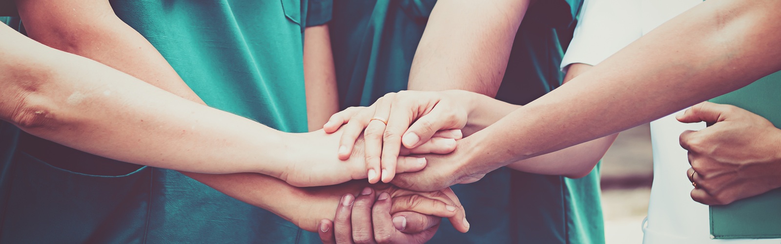 group of people in various colored scrubs stacking their hands on top of each other in a circle