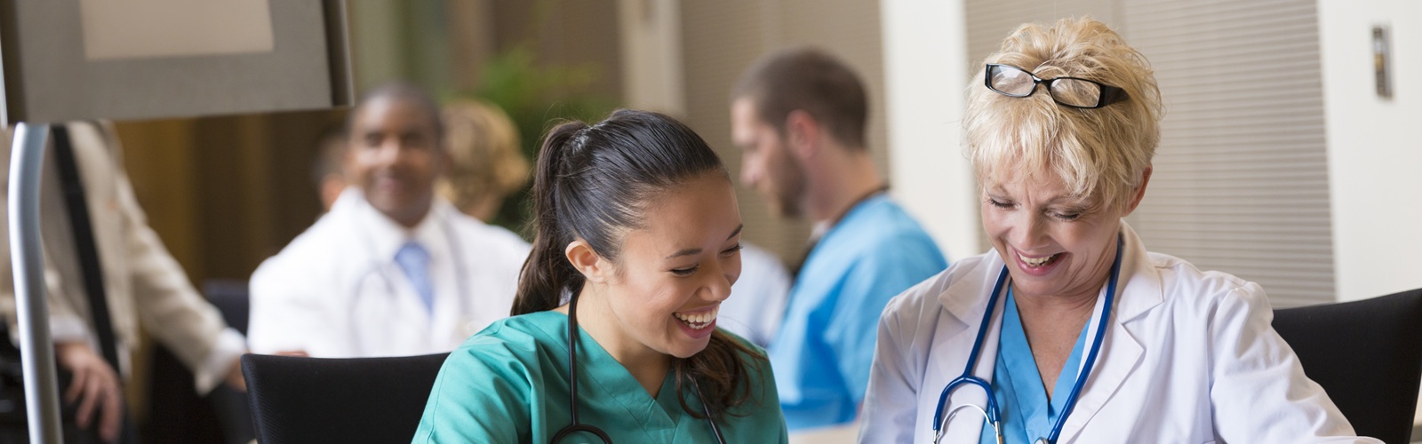 a female doctor and female nursing are looking at a notebook sitting at a long table