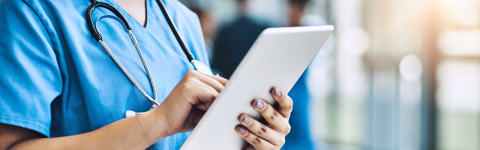 woman in blue scrubs looking at a table standing in a hallway