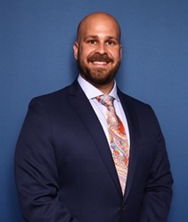 Koty Price headshot in a dark blue jacket and colorful tie