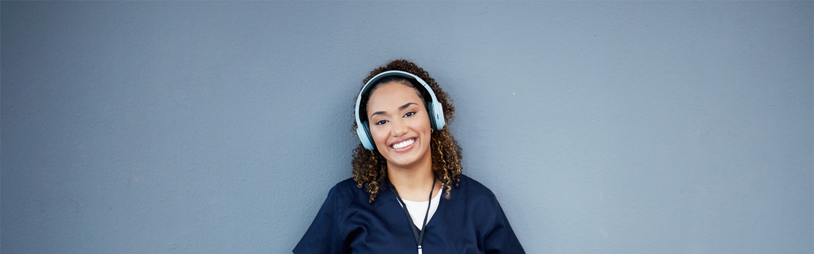 young lady with brown hair in blue scrubs sitting on the floor with a laptop in her lap
