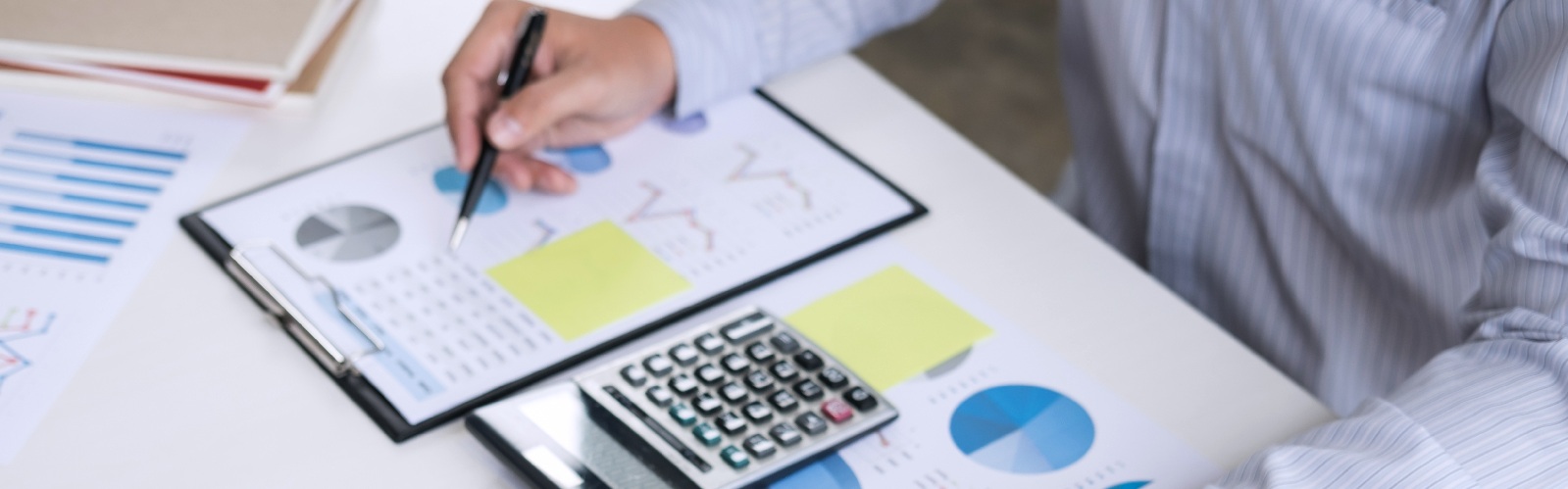 person in long sleeves typoing on a laptop while review charts on a desk