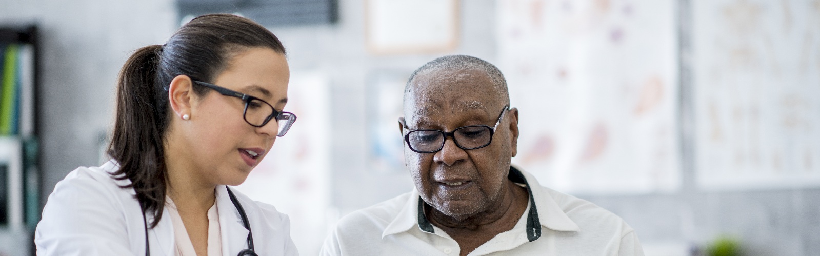 female healthcare worker wearing a white coat and stethiscope showing an older gentleman some notes on a pad