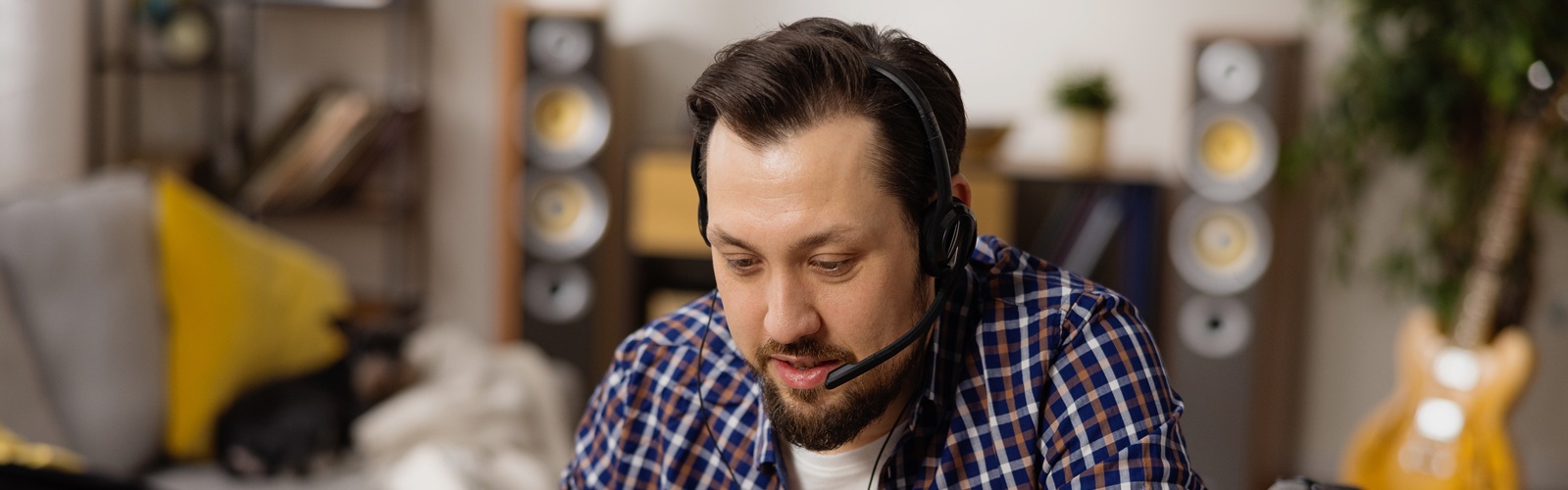 Dark-haired man with mustache, beard and headset on looking at computer