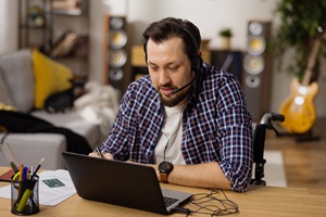 Dark-haired man with mustache, beard and headset on looking at computer