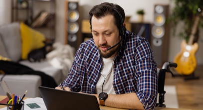 Dark-haired man with mustache, beard and headset on looking at computer