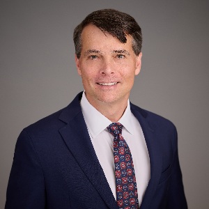 Ben DeGweck headshot in a dark suit, tie, and white shirt