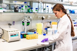 Young lady in a white lab coat with long brown hair studying a book in a pharmacy lab