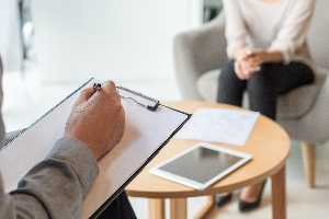 a person's hand resting on a clipboard and is sitting across another person with a table in between them