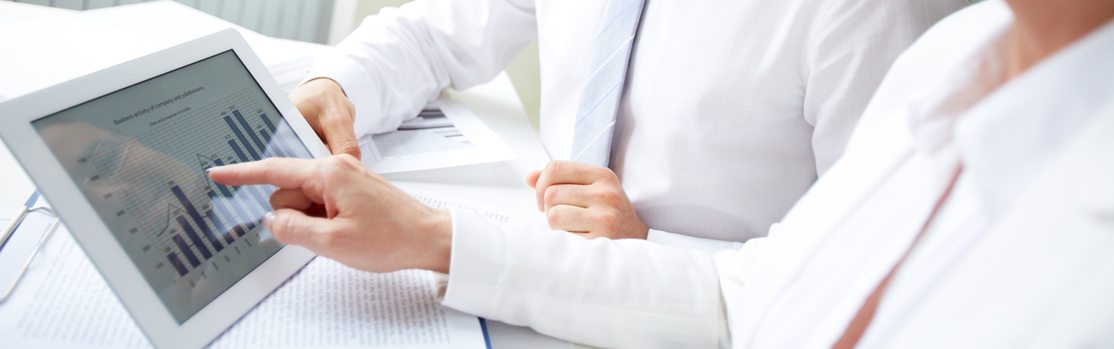 a man and a woman both in white shirts sitting together at a desk looking at a tablet screen together