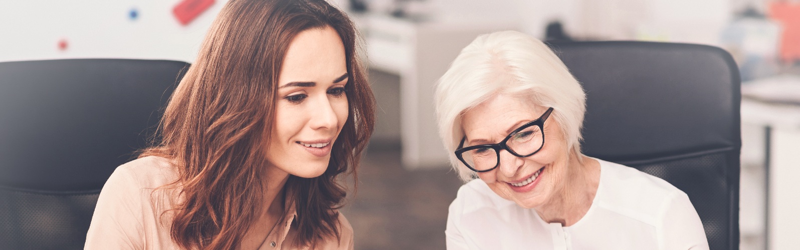 a younger and an older woman with dark glasses smiling and looking at something together