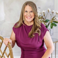 Nicole Early in a mauve dress with curled blonde hair and a flower in the background